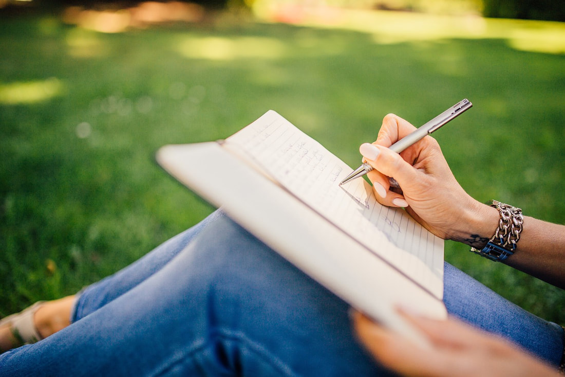 Image of a person writing in a journal in a park.